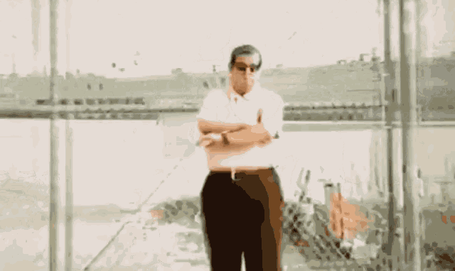 a man wearing sunglasses is standing in front of a chain link fence