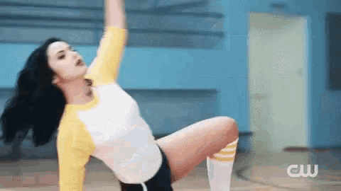a woman in a yellow and white shirt and shorts is doing a yoga pose on the floor .
