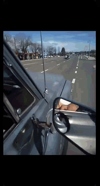 a car is driving down a road and the rear view mirror shows the driver 's reflection