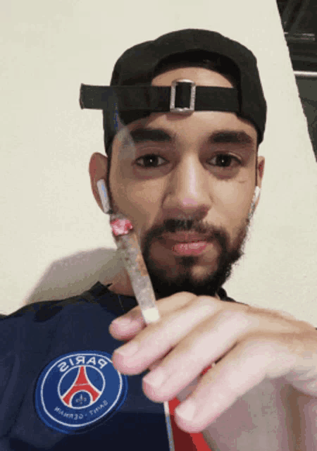 a man wearing a black hat holds a cigarette in front of his face