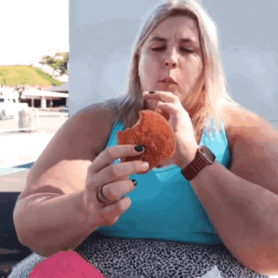 a woman in a blue tank top is eating a large donut