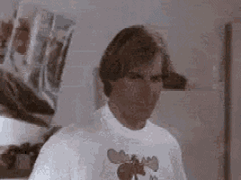 a man wearing a white t-shirt with a bee on it is standing in a room .