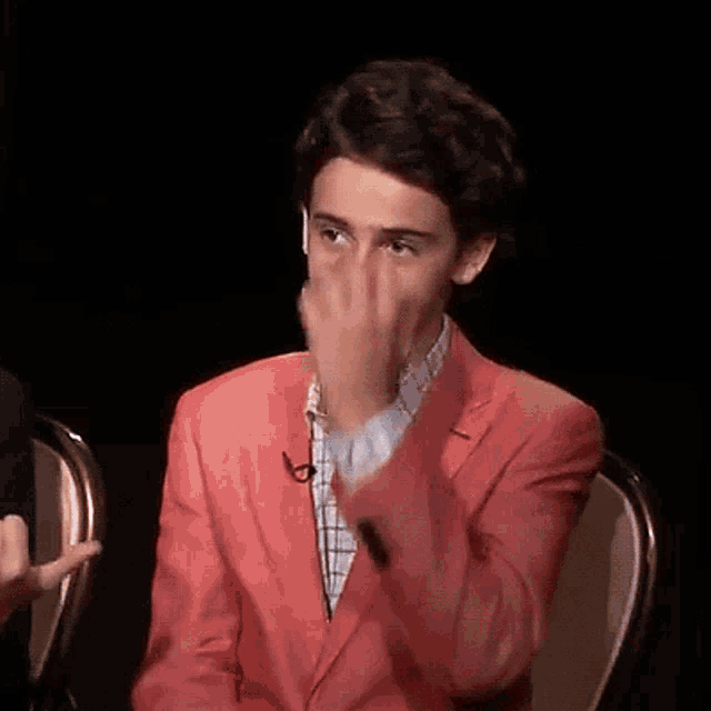 a young boy in a red suit is covering his face with his hand .