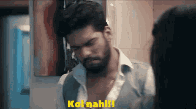 a man with a beard is looking at himself in a mirror with the words koi nahi written in yellow