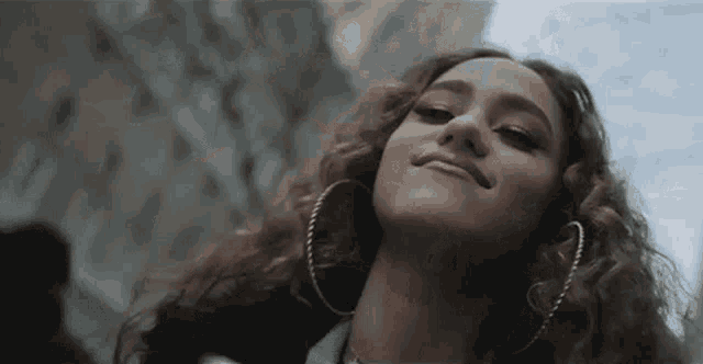 a close up of a woman with curly hair and hoop earrings smiling .