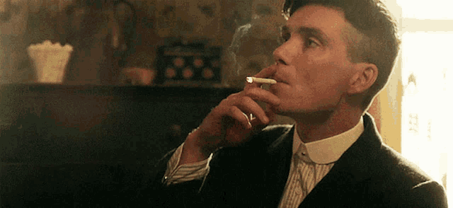 a man in a suit is smoking a cigarette in front of a window