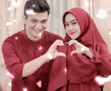 a man and a woman in red clothes are making a heart with their hands .