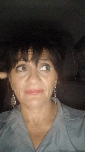 a woman wearing a gray shirt and silver earrings looks at the camera