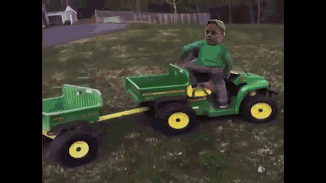 a boy is riding a john deere lawn mower pulling a trailer