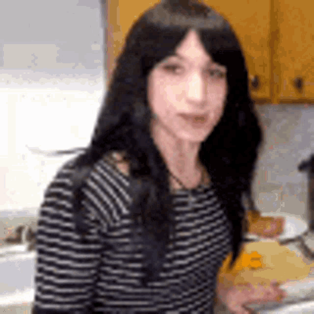 a woman with long black hair is standing in a kitchen wearing a striped shirt and a wig .