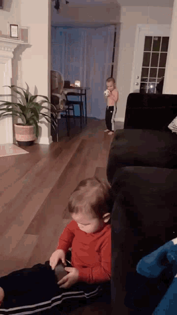 two children are playing in a living room one is sitting on the floor and the other is standing on the couch