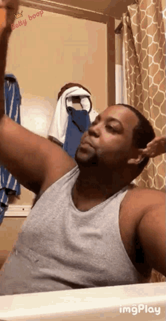 a man in a grey tank top is taking a selfie in the bathroom