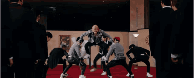 a group of young men are dancing in a room . one of the men is wearing a black leather jacket .