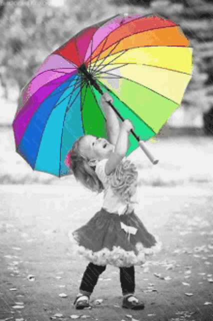 a little girl is holding up a rainbow colored umbrella in the rain