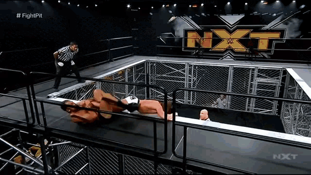 a wrestler is laying on the ground in a cage while a referee watches .