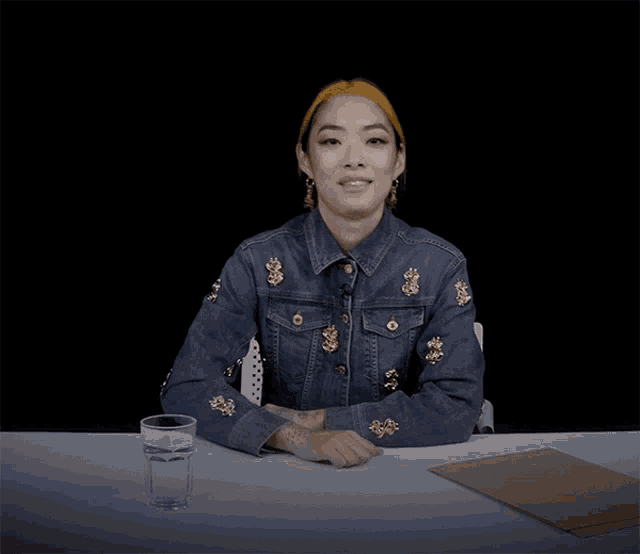 a woman in a denim jacket sits at a table with a glass of water on it