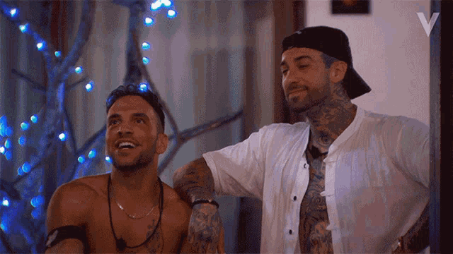 two shirtless men are standing next to each other and one has a tattoo on his arm