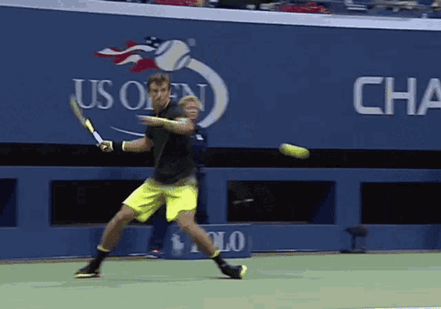 a man swings a tennis racket at a tennis ball in front of an us open sign