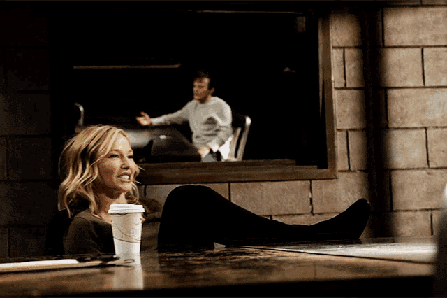 a woman sits at a table with her legs crossed and a cup of coffee in her hand