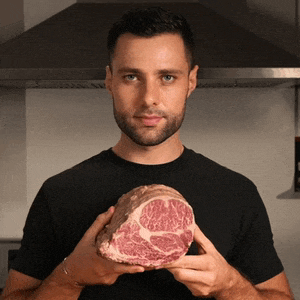 a man in a black shirt holds a large piece of meat