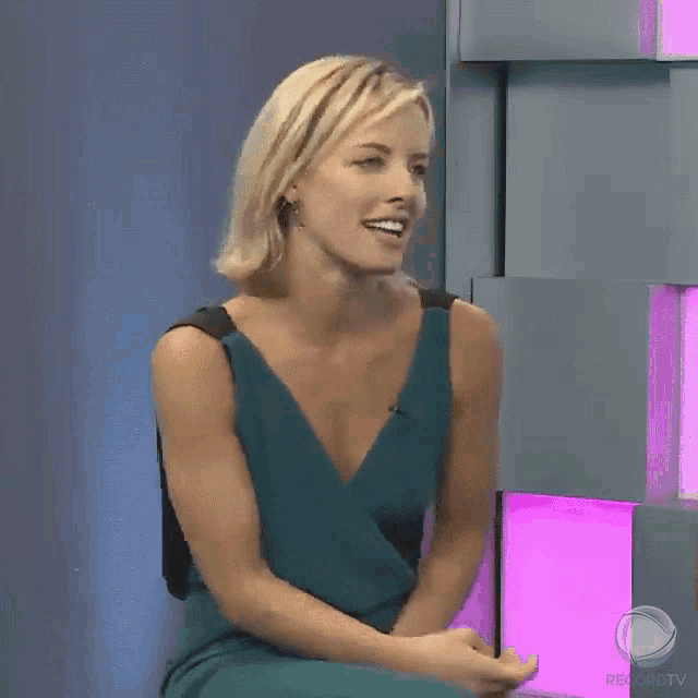 a woman in a green dress is sitting in front of a sign that says rekordtv