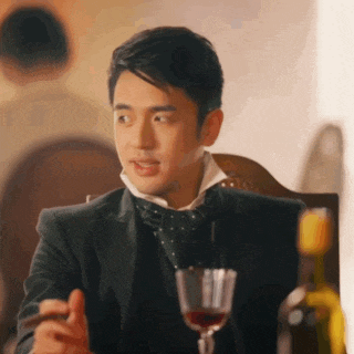 a man in a suit and bow tie is sitting at a table with a glass of wine and a bottle of wine .