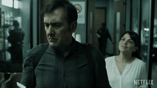 a man and a woman are walking down a hallway with netflix written on the bottom of the screen