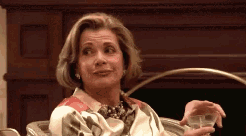 a woman is sitting in a chair holding a glass of wine and making a funny face .