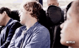 a group of people are sitting on a bus with a netflix logo on the bottom of the screen .