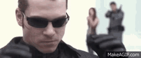 a man wearing sunglasses is pointing a gun at a woman .
