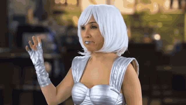 a woman wearing a white wig and silver gloves is waving