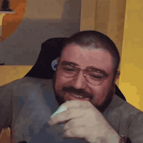 a man with a beard and glasses is laughing and covering his mouth with his hands .