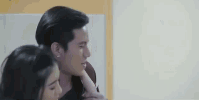 a man and a woman are sitting next to each other in a room and the woman is touching the man 's face .