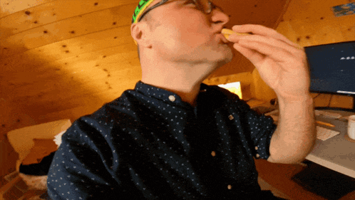 a man wearing glasses and a blue shirt is eating a piece of food