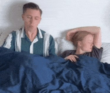 a man and a woman are sleeping in a bed with blue sheets .