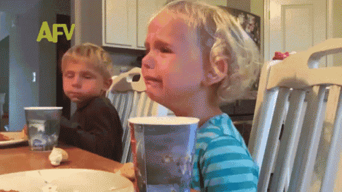 a little girl is crying while sitting at a table with a cup in front of her ..