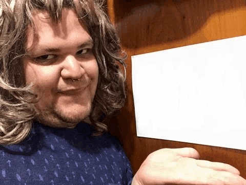 a man wearing a wig and a nose ring is holding a white piece of paper