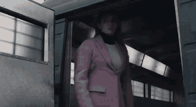 a woman in a pink coat is standing in a doorway .