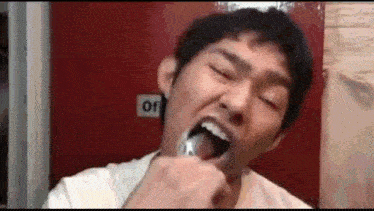 a man is brushing his teeth in front of a red door with his mouth open .