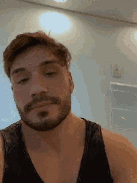 a close up of a man with a beard wearing a black tank top .