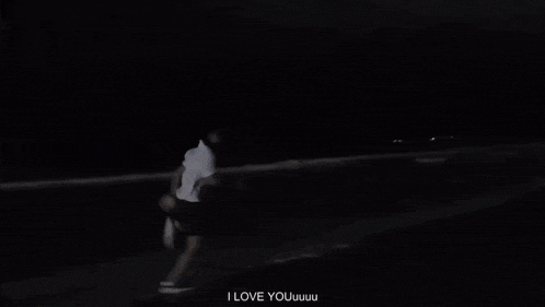 a man in a white shirt is standing on a beach at night .