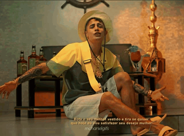 a man wearing a yellow shirt and white shorts is sitting in front of a table with bottles of alcohol on it