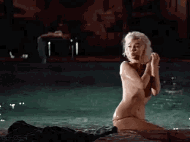 a naked woman is kneeling in a swimming pool at night .