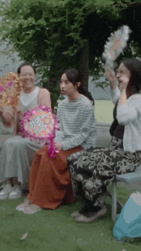 a group of women are sitting on a bench holding fans and one of them is holding a fan that says i love you