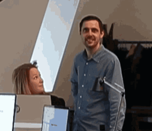 a man in a blue shirt stands next to a woman in front of a computer monitor