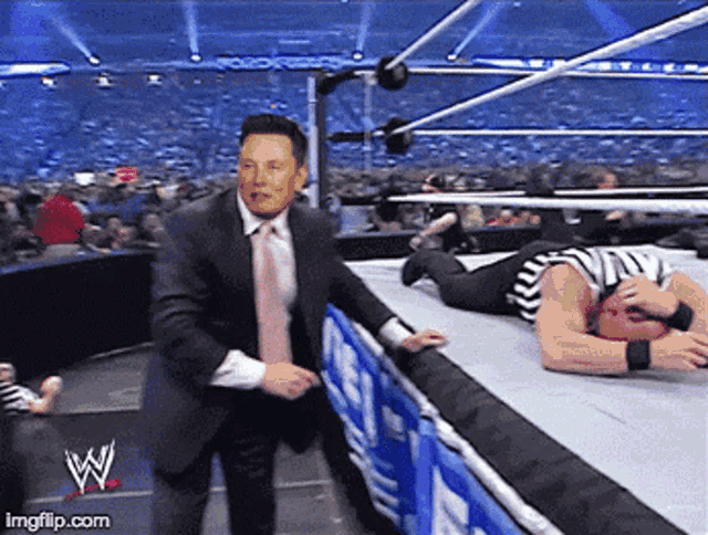 a man in a suit and tie stands next to a referee in a wrestling ring