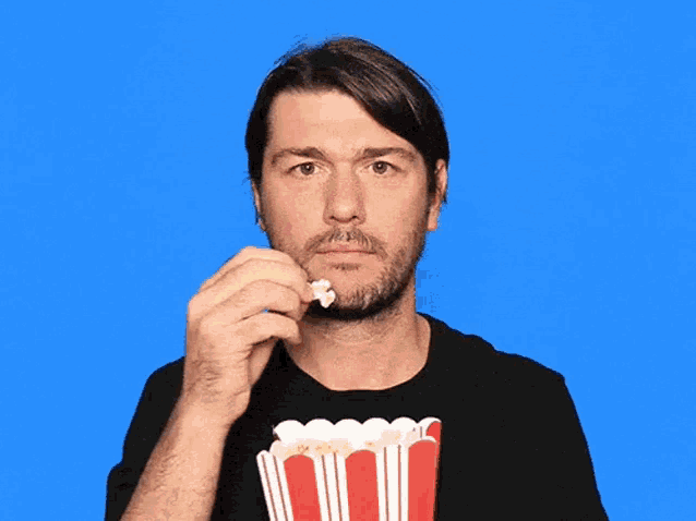 a man in a black shirt is eating popcorn from a red bucket .