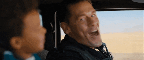 a man is laughing while sitting in the back seat of a car next to a child .