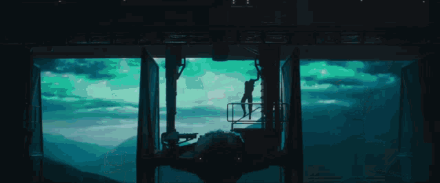 a silhouette of a man standing on a balcony looking out over a mountain range