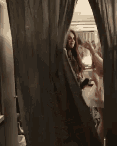 a woman is standing in a room behind a curtain and holding a glass of wine .